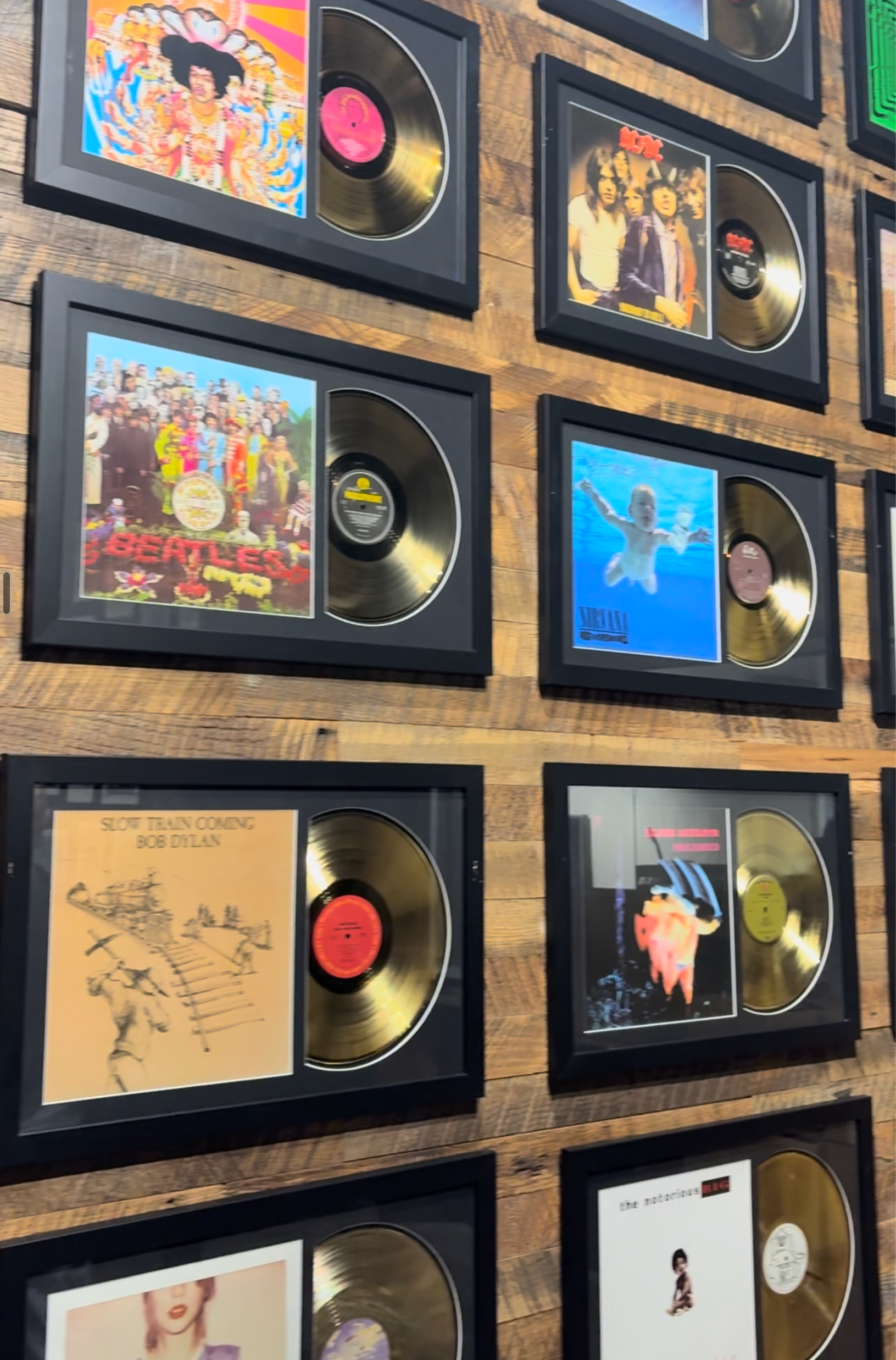 A grid of framed gold vinyl record plaques with colorful album covers, arranged on a wooden surface. 